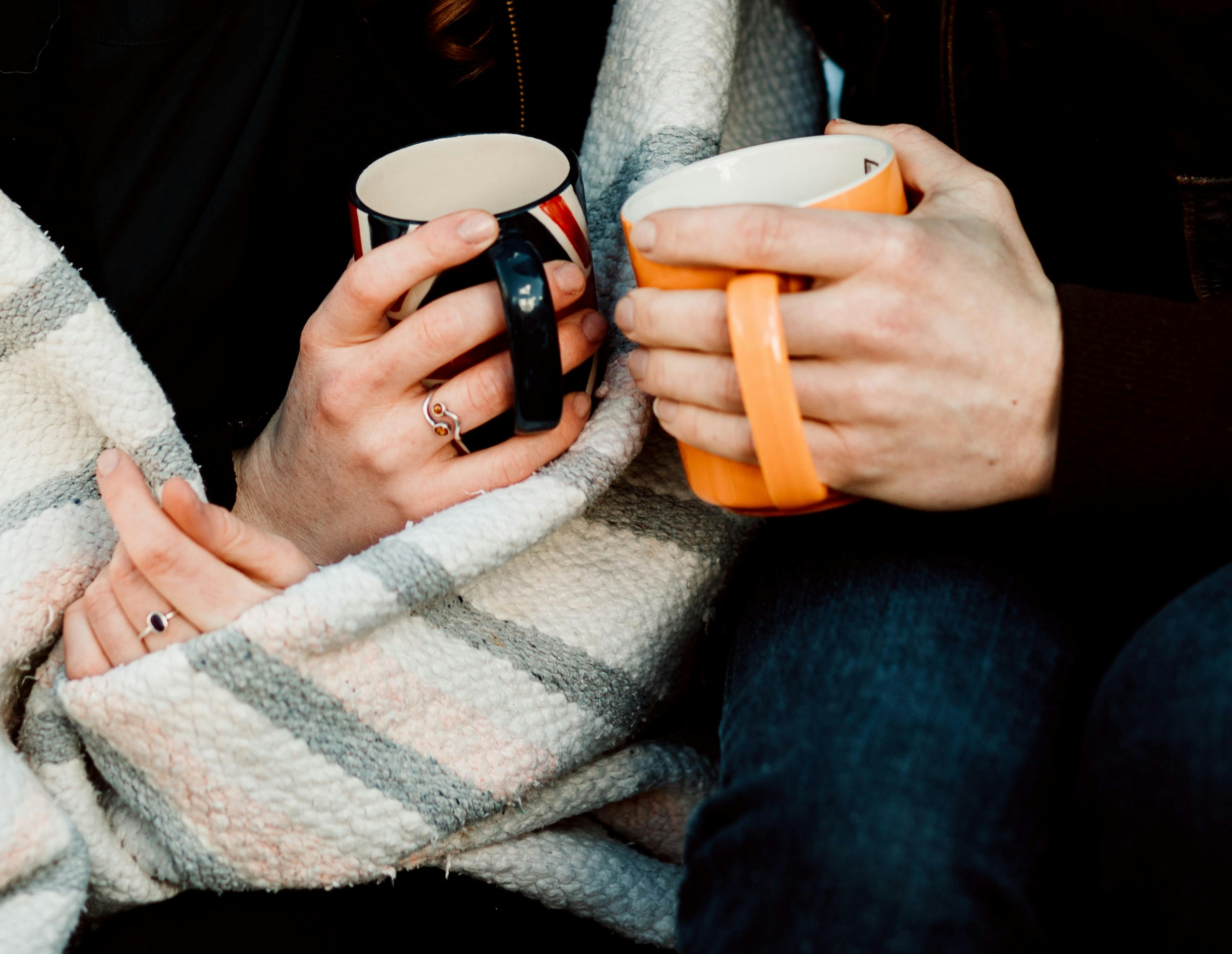 two people holding mugs wrapped in blankets