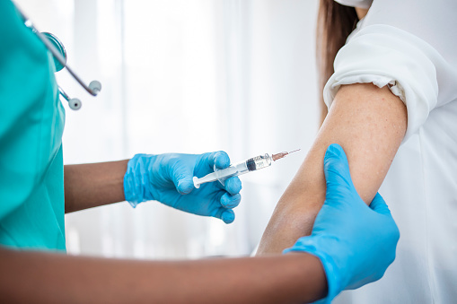 an image of a person in a white shirt receiving a vaccination from a medical professional wearing blue gloves
