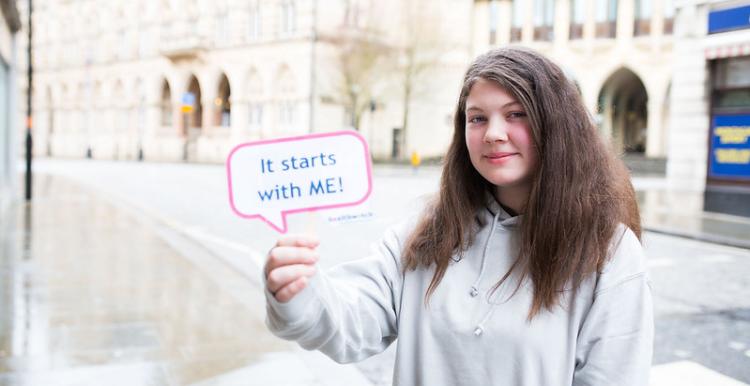 Picture of girl holding up a sign that reads 'It starts with ME'