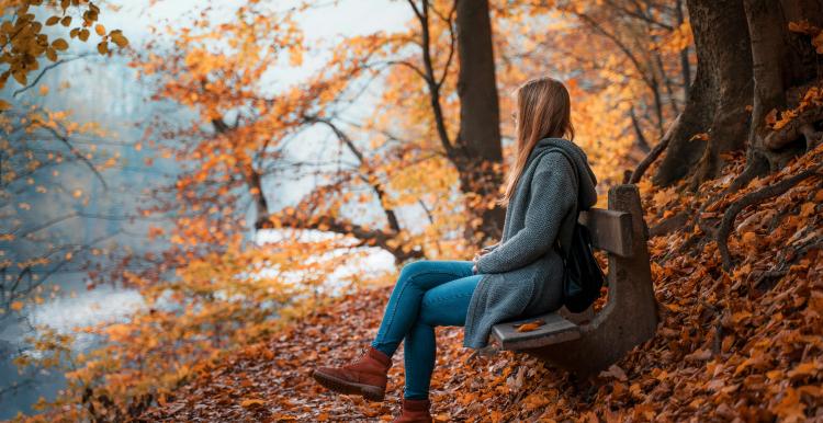 lady sat on a bench in an autumn scene