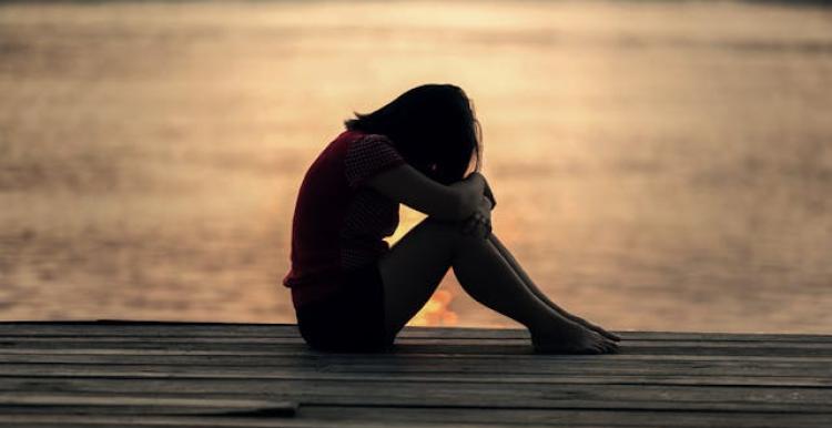 Girl sat by the water with her head on her knees