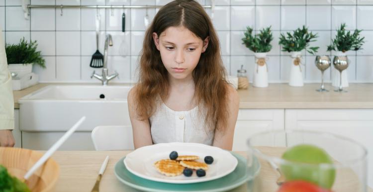 Young girl looking sadly at a plate of food