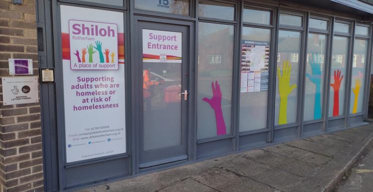 The picture is of the outside of a one storey building. There is text on the door saying "Shiloh" and pictures of multi coloured hands on the windows. 