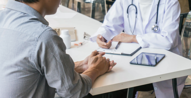 a photo of a healthcare professional sitting on a table with a patient. on the table is a clipboard, tablet and medication