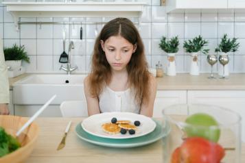 Young girl looking sadly at a plate of food