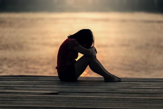 Girl sat by the water with her head on her knees