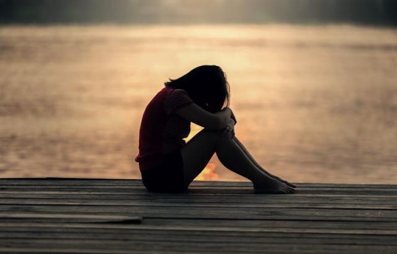 Girl sat by the water with her head on her knees